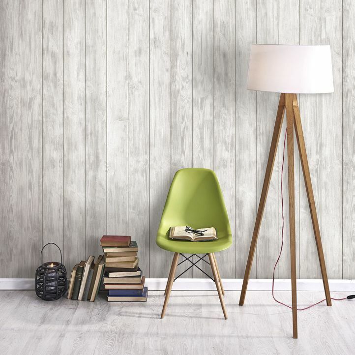 Revestimiento de pared de pvc en lamas con un diseño de madera gris instalado en una pared con una silla, libros y una lámpara.