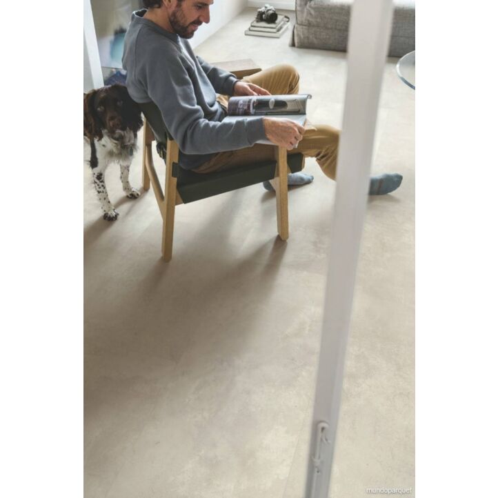 Suelo laminado de Quick-Step de la colección Muse Hormigón Moteado instalado en un ambiente de salón con un hombre leyendo y un perro visto de más cerca