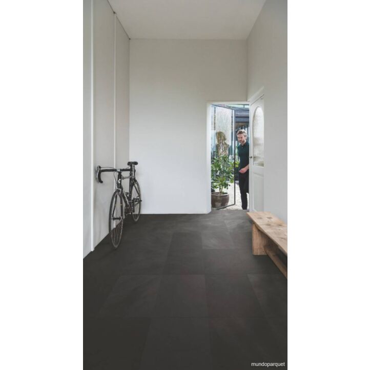 Suelo laminado de Quick-Step de la colección Muse Pizarra Negra instalado en un recibidor con una bicicleta y un hombre entrando