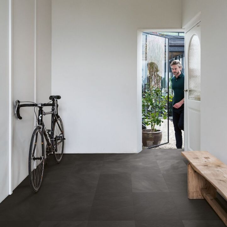 Suelo laminado de Quick-Step de la colección Muse Pizarra Negra instalado en un recibidor con una bicicleta y un hombre entrando