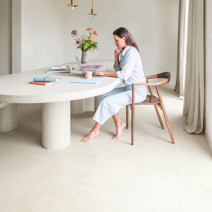 Suelo laminado de Quick-Step de la colección Muse Tiza instalado en un salón con una mujer sentada en una silla leyendo