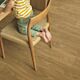 Suelo laminado de la marca Quick-step de la serie CLASSIC Roble Tostado instalado en un salón con una silla y un niño descalzo