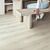 Suelo laminado de la marca Quick-step de la serie CLASSIC Roble Gris Ceniza instalado en un salón con un banquete y una persona sentada.