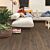 Suelo laminado de la marca Quick-step de la serie CLASSIC Roble marrón cacahuete instalado en un salon con gente en un sofá.